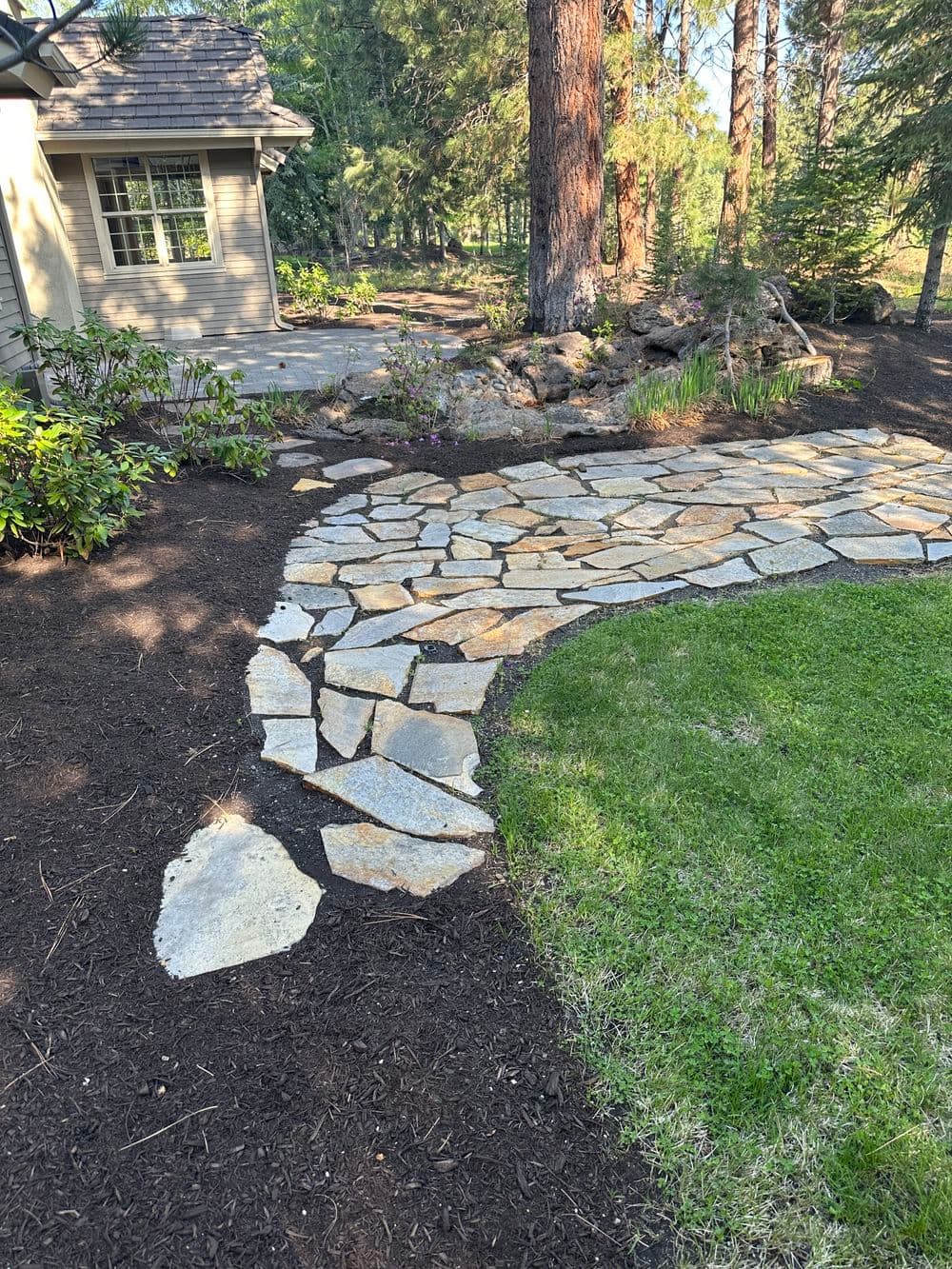 Natural stone pathway winding through a landscaped garden with trees and shrubs.